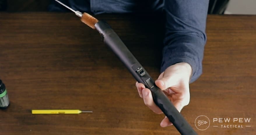 Use your cleaning brush pushing from the rear of the shotgun forward