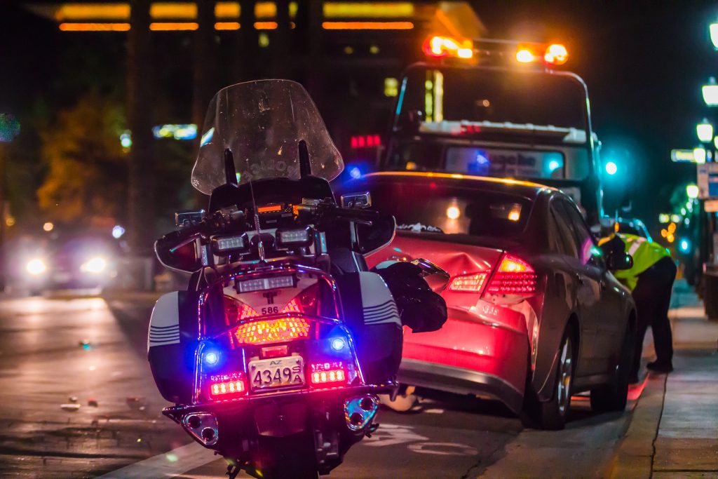 Police motorcycle and a crashed car being hooked up to a tow truck